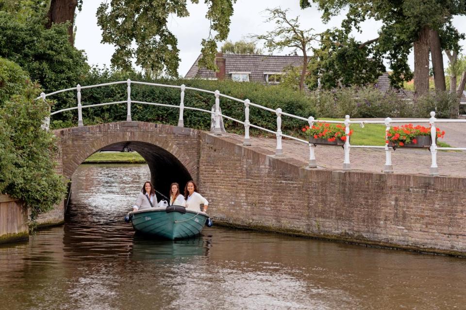 drie vrouwen bootje varen en op de achtergrond een stenen brug
